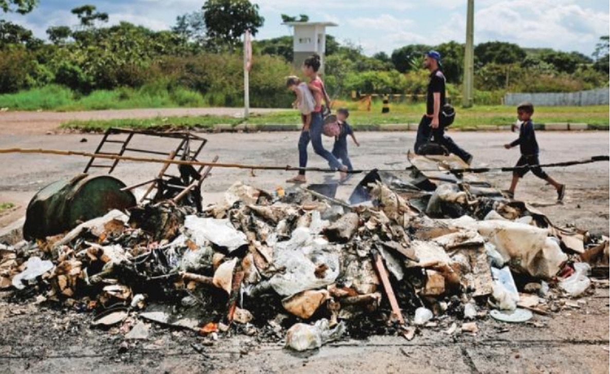 Una familia de venezolanos pasa frente a los restos de un campamento de inmigrantes que fue quemado por residentes de la ciudad brasileña de Paracaima. (NACHO DOCE. REUTERS)