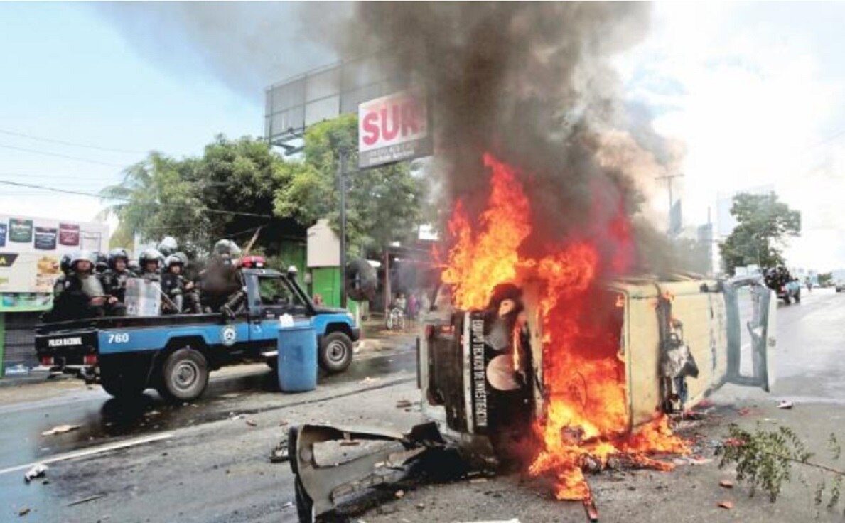 Agentes antidisturbios viajan frente a un automóvil de la policía en llamas, durante una protesta contra el gobierno del presidente nicaragüense Daniel Ortega en Managua, Nicaragua. (OSWALDO RIVAS. REUTERS)