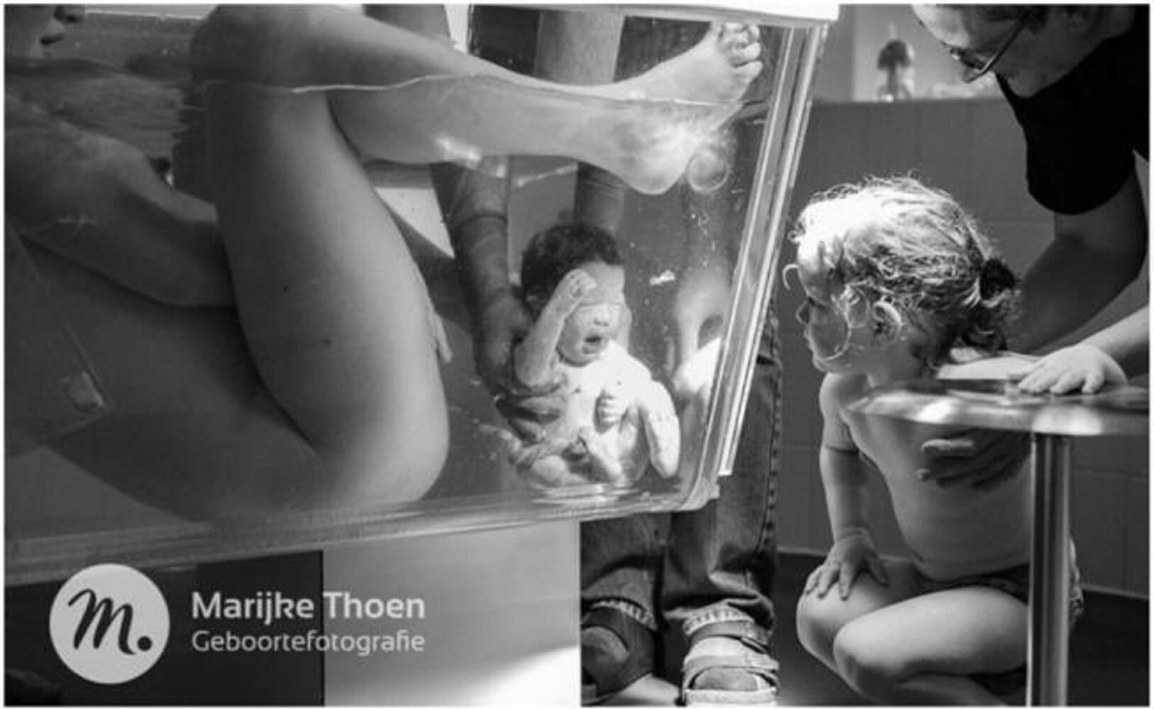 En la imagen, se puede ver al bebé en el momento de llegar al mundo mientras su hermana lo observa todo al otro lado del cristal de la bañera